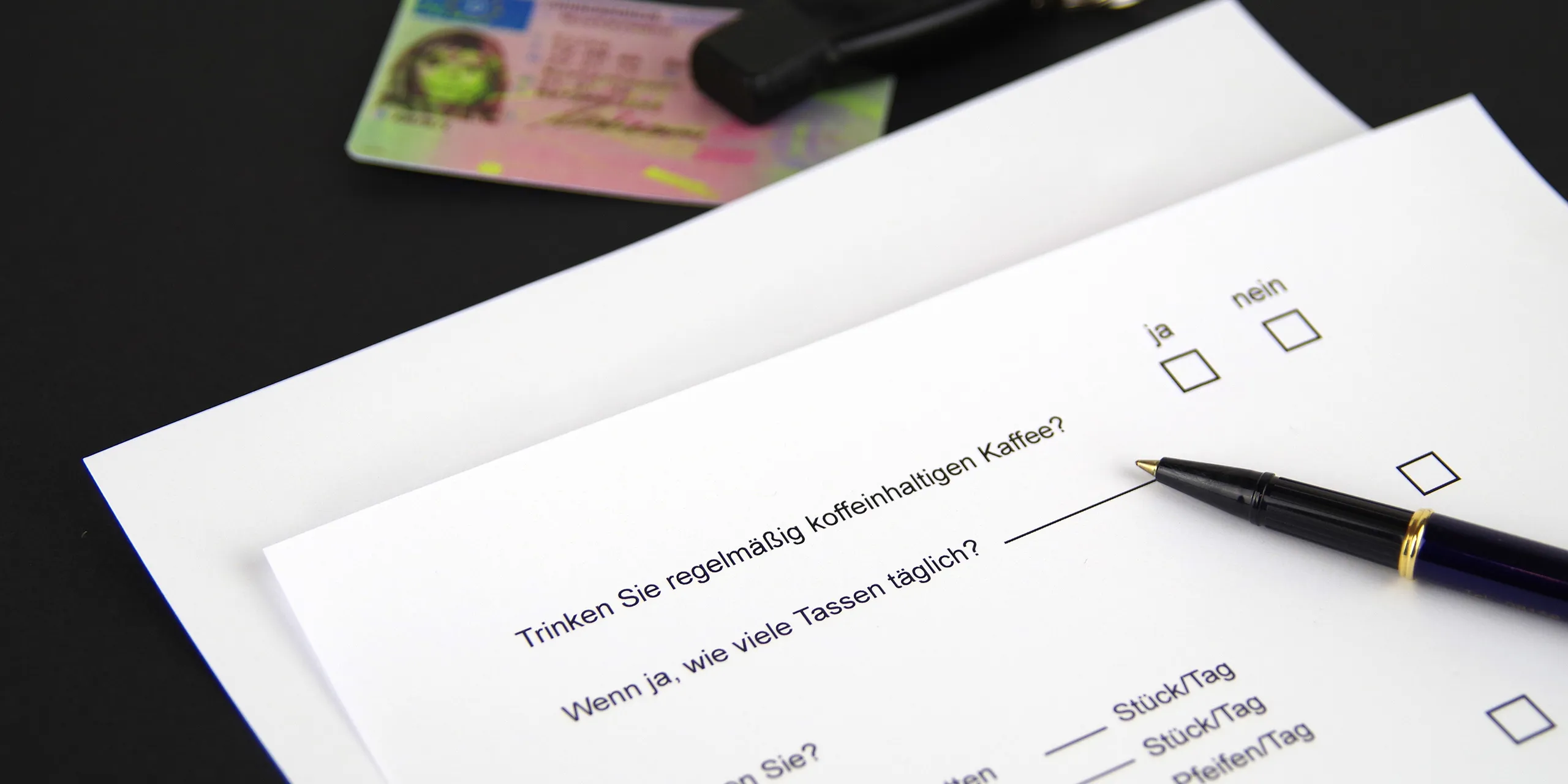 Ein Formular für eine Untersuchung liegt auf einem Tisch, daneben ein Führerschein und ein Stift.
