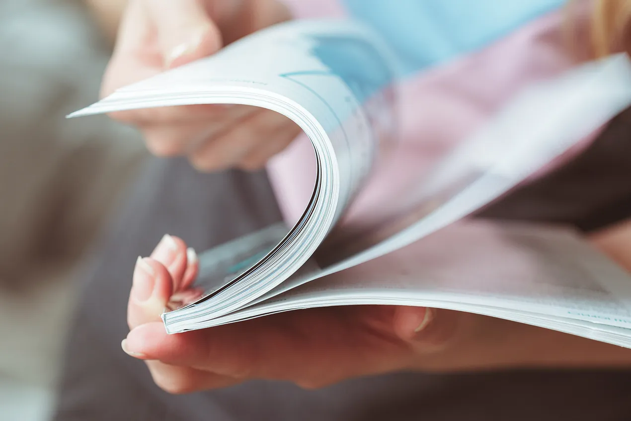Eine Person blättert durch ein Magazin, das in der Hand gehalten wird.