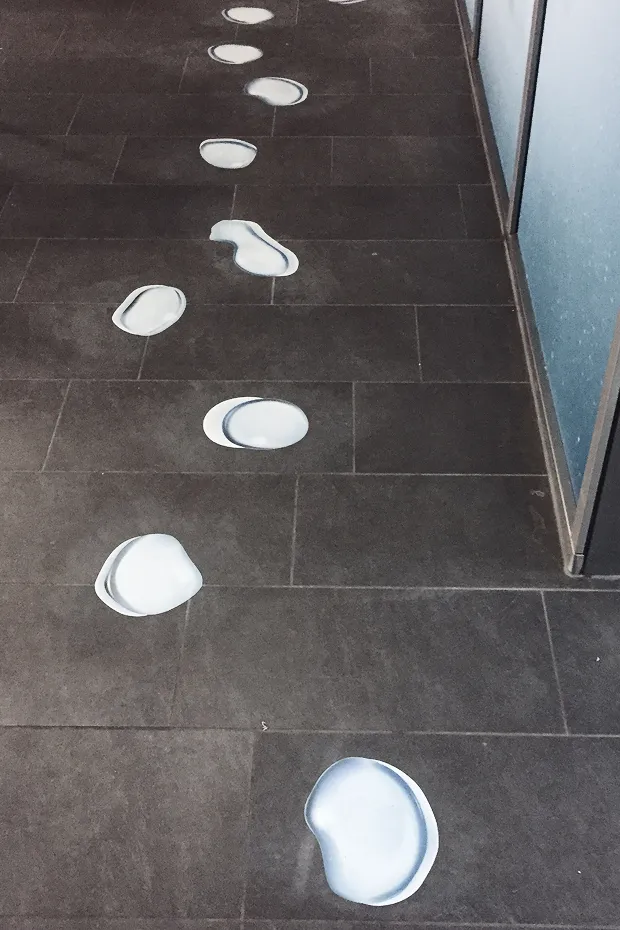 Helle Tropfen auf einem dunklen Fliesenboden, die einen Weg markieren.
