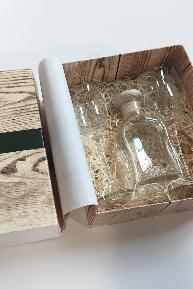 Eine geöffnete Geschenkbox mit einer transparenten Flasche auf einem Bett aus Stroh.