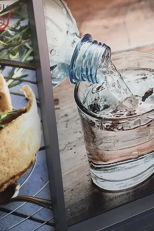 Eine Wasserflasche gießt Wasser in ein Glas, das auf einem Tisch steht. Im Hintergrund ist ein Gericht sichtbar.