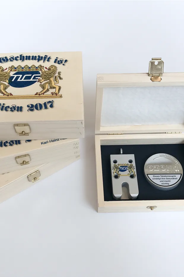 Holzkiste mit Deckel, darin ein silberner Medaille und ein Gerät mit blauen und grauen Elementen.