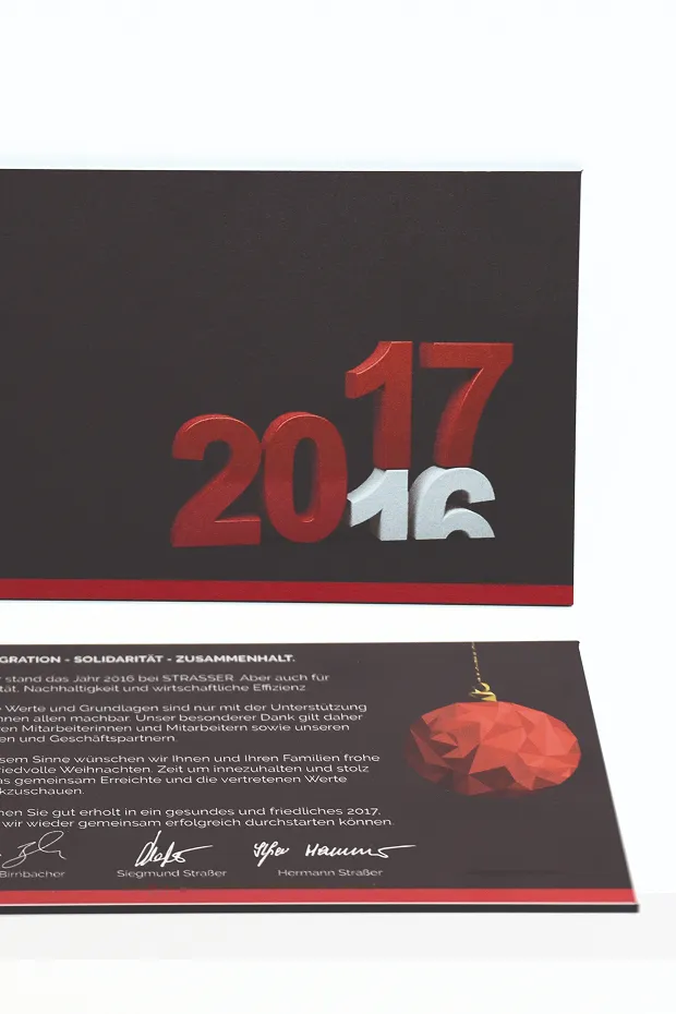 Eine Karte mit den Jahreszahlen 2016 und 2017 in rot und silber, dekoriert mit einer roten Weihnachtskugel.